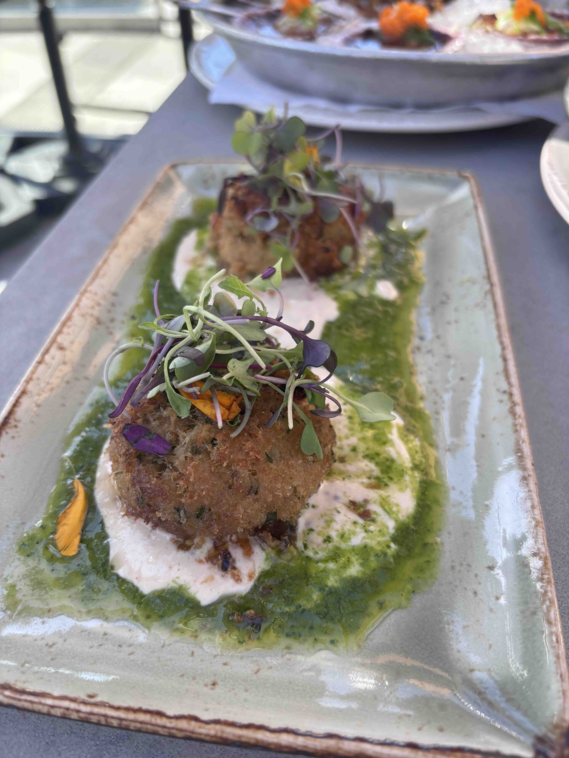 crab cakes plated on a green sauce with microgreen garnish
